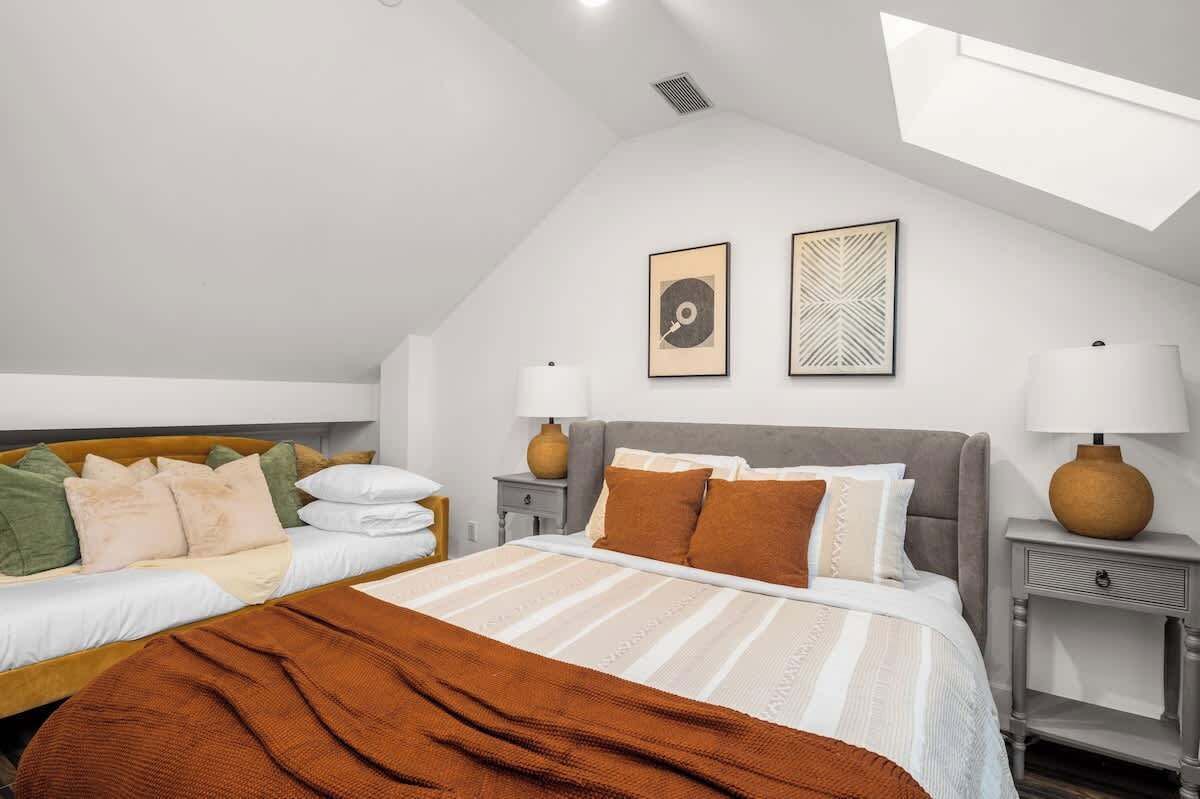 A bedroom with two beds, a skylight, and two wall-mounted lamps.