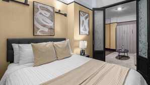 A hotel room with a large bed, two wall-mounted lamps, and abstract art on the walls. - Central Midtown 1BR | Walk to Times Square! (New York)