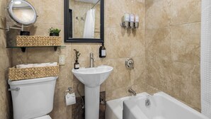 A bathroom with a toilet, sink, and bathtub. There is a mirror above the sink and a showerhead above the bathtub. - Central Midtown 1BR | Walk to Times Square! (New York)