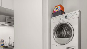 Un lavadero con dos lavadoras de carga frontal apiladas, una cesta de detergente y un lavabo con grifo.