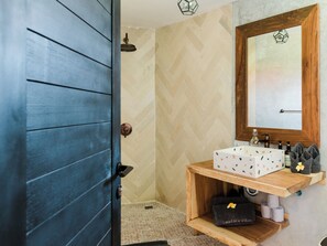 Een badkamer met een houten deur, een spiegel met een honingraatvormig frame, een wastafel met een behangpatroon en een handdoekhouder met handdoeken.