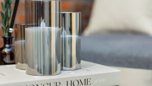 Ein Buch mit dem Titel "Moncur Home at 1000" und ein weiteres Buch mit dem Titel "Moncur Home" stehen auf einem Tisch, zusammen mit einer Kerze.