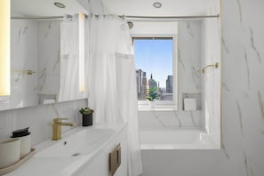 A modern bathroom with a large mirror, a bathtub, and a window with a city view.