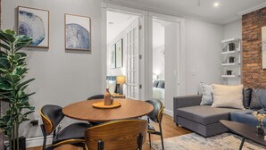 Un salon moderne avec une table à manger ronde en bois, un canapé gris et un mur d’accent en briques.