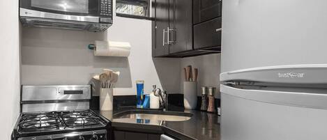 Una cocina compacta con armarios oscuros, electrodomésticos de acero inoxidable, incluyendo estufa, microondas y lavavajillas, además de un refrigerador.