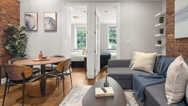 Un salon moderne comprenant un coin repas, un canapé gris et un mur décoratif en briques.