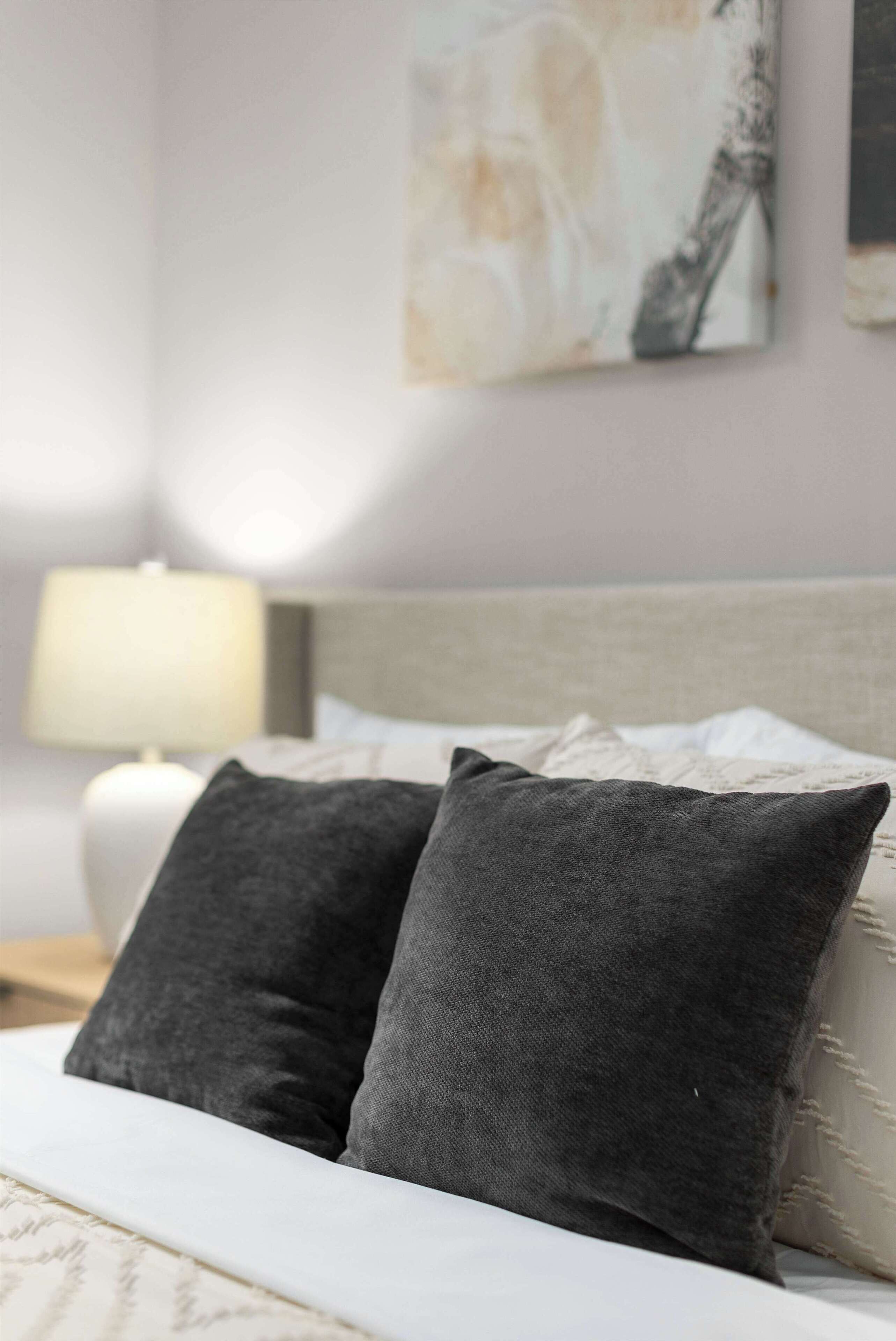A bed with two dark pillows, a white headboard, and a lamp on a bedside table.