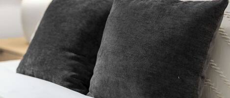 A bed with two dark pillows, a white headboard, and a lamp on a bedside table.