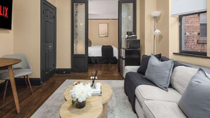 A modern hotel room with a bed, a sofa, a coffee table with flowers, a TV, and a desk with a lamp. - Premier Midtown Stay | Walk to Times Square! (New York)