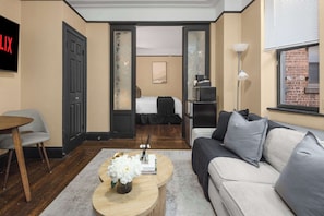 A modern hotel room with a bed, a sofa, a coffee table with flowers, a TV, and a desk with a lamp.