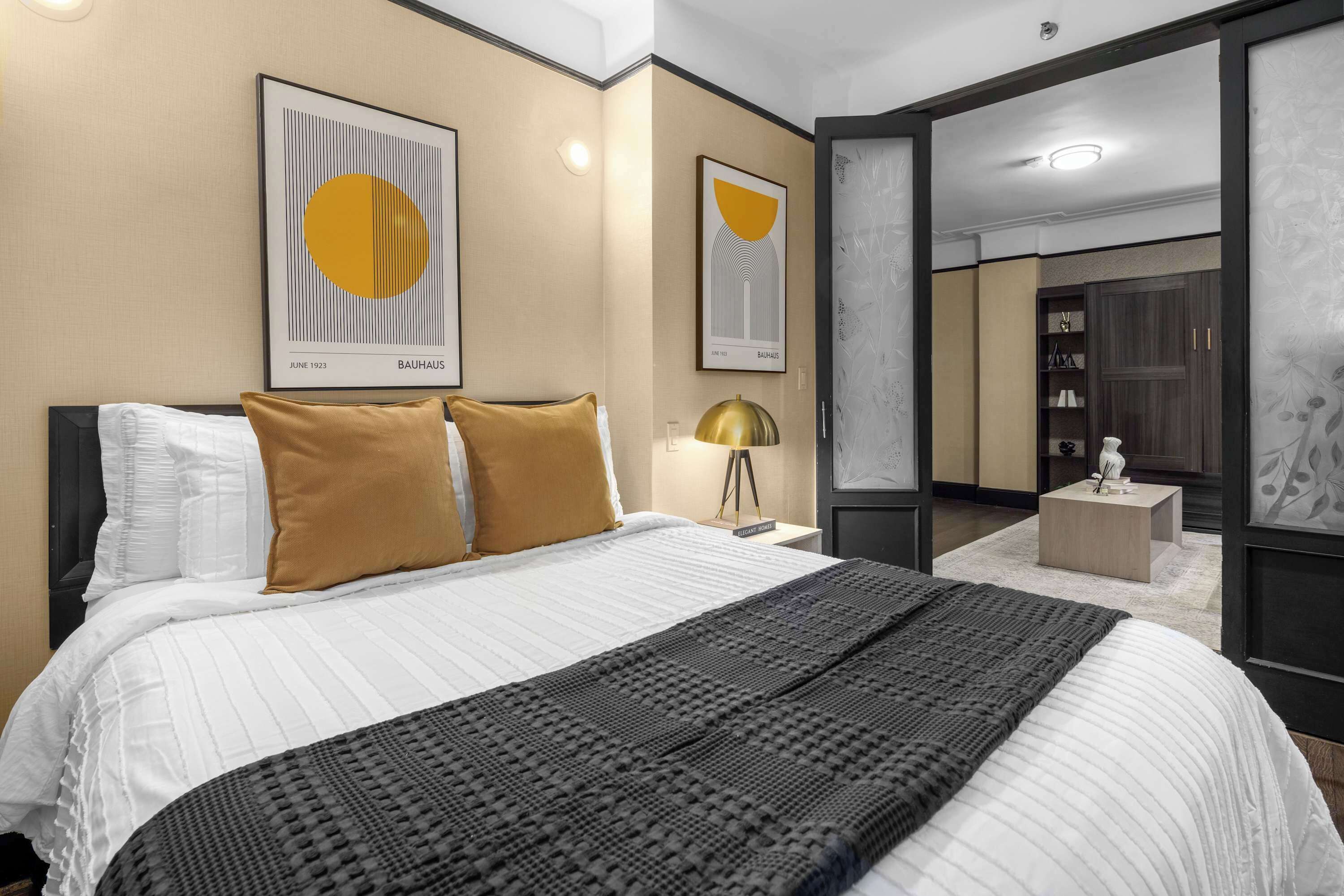 A modern hotel room with a large bed, two pillows, a bedside lamp, and artwork on the walls.