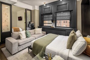 Quarto de hotel com cama, sofá, televisão e janela com persianas.