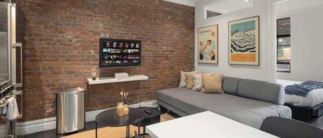 A modern living room with a brick wall, a gray sofa, a white table, and a mounted TV.