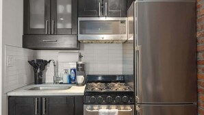 A compact kitchen with dark cabinets, a stainless steel refrigerator, a built-in microwave, a gas stove, and a dishwasher. - Chic 2BR Retreat in the Heart of Times Square (New York)