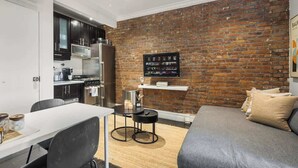 A modern kitchen with dark cabinets, a brick wall, and a flat-screen TV mounted above a shelf. - Chic 2BR Retreat in the Heart of Times Square (New York)