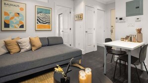 A modern living room with a grey sofa, a dining table with chairs, and artwork on the walls. - Chic 2BR Retreat in the Heart of Times Square (New York)