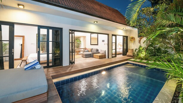 Una casa moderna con piscina, puertas de cristal amplias que dan a una sala de estar y un jardín cuidado.