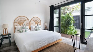 Un dormitorio con una cama grande, un cabecero de madera, una mesita de noche con una lámpara y vistas a un jardín a través de una puerta corredera.