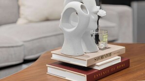 Uma escultura de cerâmica branca sobre uma mesa de madeira com livros, incluindo 'Savoir Vivre' e 'Essence of Home'.
