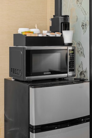 Un four à micro-ondes est posé sur le dessus d’un réfrigérateur, à côté duquel se trouvent une machine à café, ainsi que quelques tasses et assiettes.