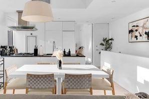 A modern kitchen with white cabinetry, a dining area with a white table and woven chairs, and a large pendant light.
