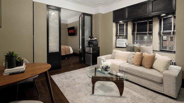 Un salon moderne avec une table basse en verre, un canapé beige et un téléviseur fixé au mur.