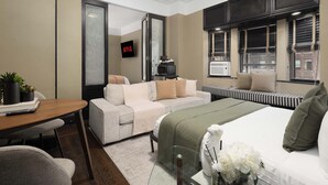 Une chambre d’hôtel moderne équipée d’un canapé, d’un lit, d’une télévision et d’une fenêtre avec des stores.