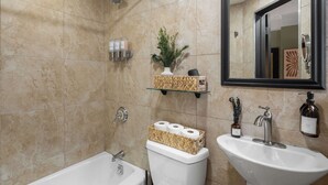 Une salle de bain avec une baignoire, des toilettes et un lavabo. On y trouve des articles de toilette accrochés au mur et un miroir au-dessus du lavabo.