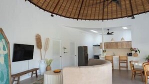Un soggiorno moderno con un divano curvo, una televisione a schermo piatto, un'area pranzo con sedie in legno e una cucina con pensili e frigorifero.