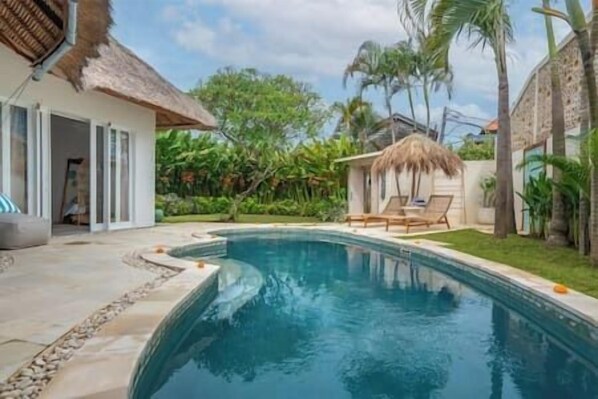 A swimming pool with a thatched roof structure, surrounded by lush greenery and palm trees. - NEW Private Full-Time Butler / 7 Min Walk to Beach (Seminyak)
