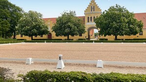 A large open riding arena with a yellow building in the background. - Beautiful home in Flyinge with WiFi (Flyinge)