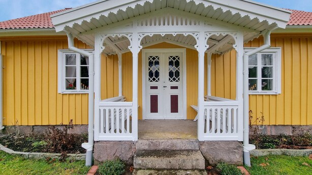 A yellow building with a white porch and a double door with glass panels. - 3 bedroom beautiful home in Broaryd (broaryd)