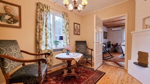 A room with a wooden floor, a round table with a white tablecloth, two upholstered chairs, a red patterned rug, and a chandelier. - 3 bedroom beautiful home in Broaryd (broaryd)