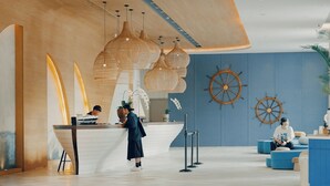 Un vestíbulo moderno con mostrador de recepción, ruedas de barco de madera en la pared y una zona de estar con cojines azules.