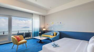 A modern hotel room with a large bed, a sofa, a chair, and a view of the sea.