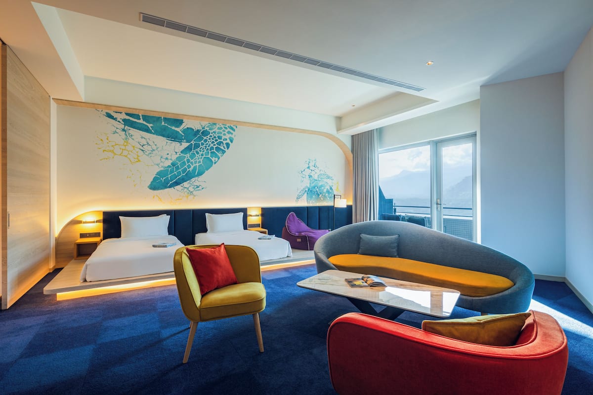 A modern hotel room with a bed, a sofa, a chair, and a coffee table.