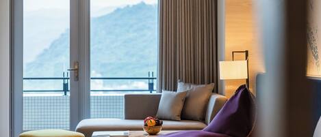Habitación de hotel con sofá, una mesita con un cuenco de fruta, un sillón morado y vistas a las montañas a través de una puerta corredera.