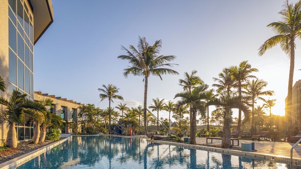 Una piscina rodeada de palmeras y un edificio moderno.