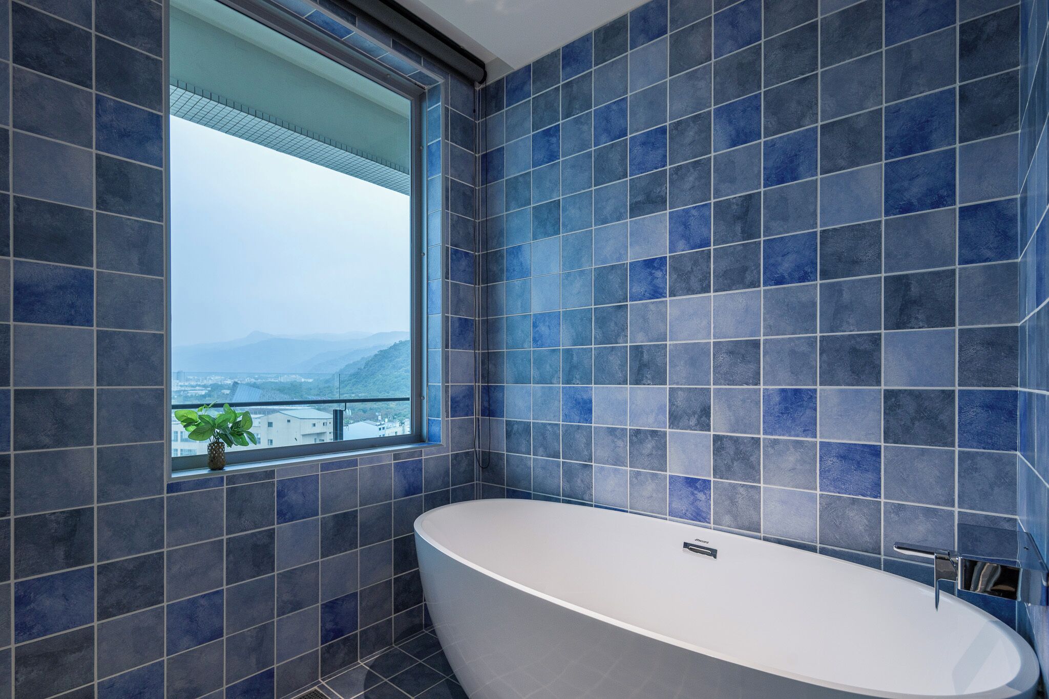 Une salle de bain moderne avec une grande baignoire, des carreaux bleus et une fenêtre donnant sur les montagnes.