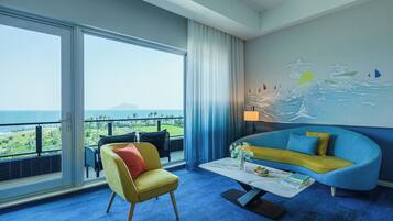 Una habitación de hotel con un ventanal grande, un sofá azul, un sillón amarillo y un mural de surfistas en la pared.