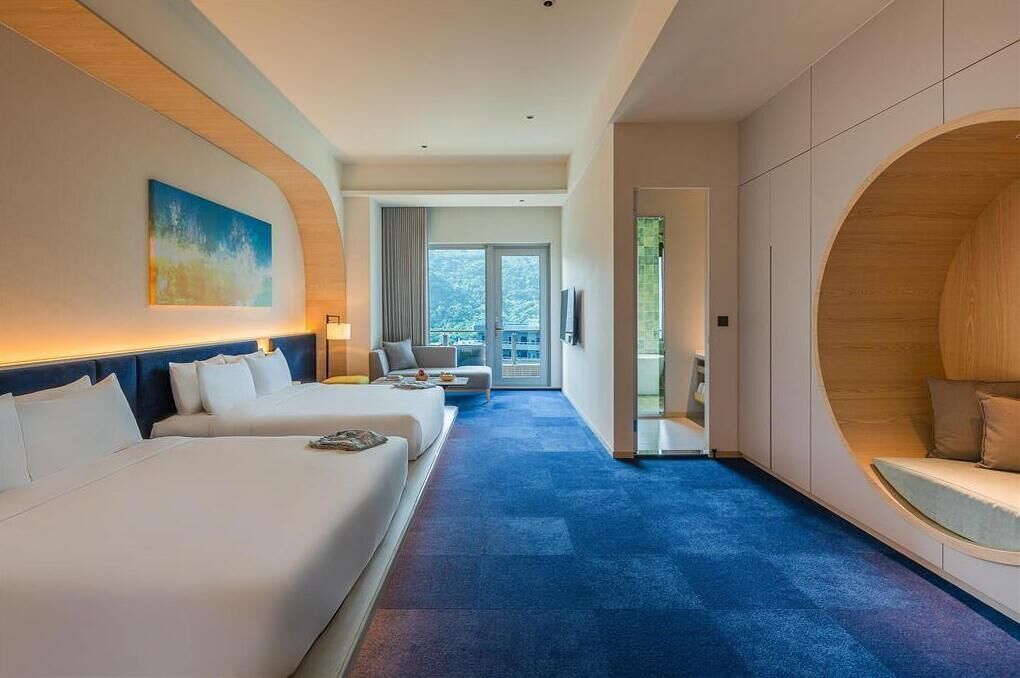 A hotel room with two beds, a sofa, a large window, and a view of the outdoors.