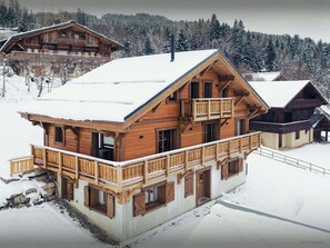 A large wooden chalet with multiple balconies and a snow-covered roof, surrounded by a forested mountain area. - Chalet Alpage du Bettex - Bright and airy chalet with sauna - OVO Network (Saint-Gervais-les-Bains)