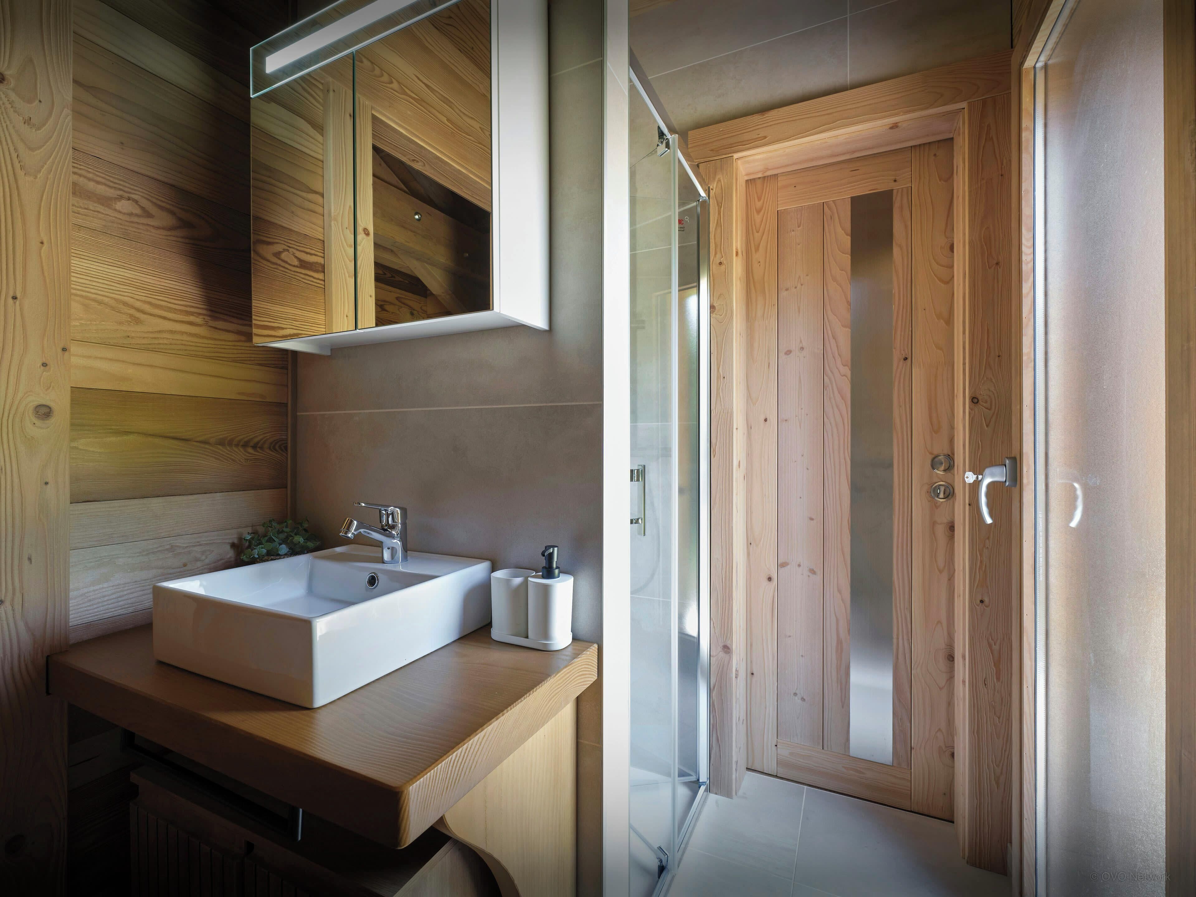 A modern bathroom with a wooden vanity, a large mirror, a white sink, and a glass shower enclosure.