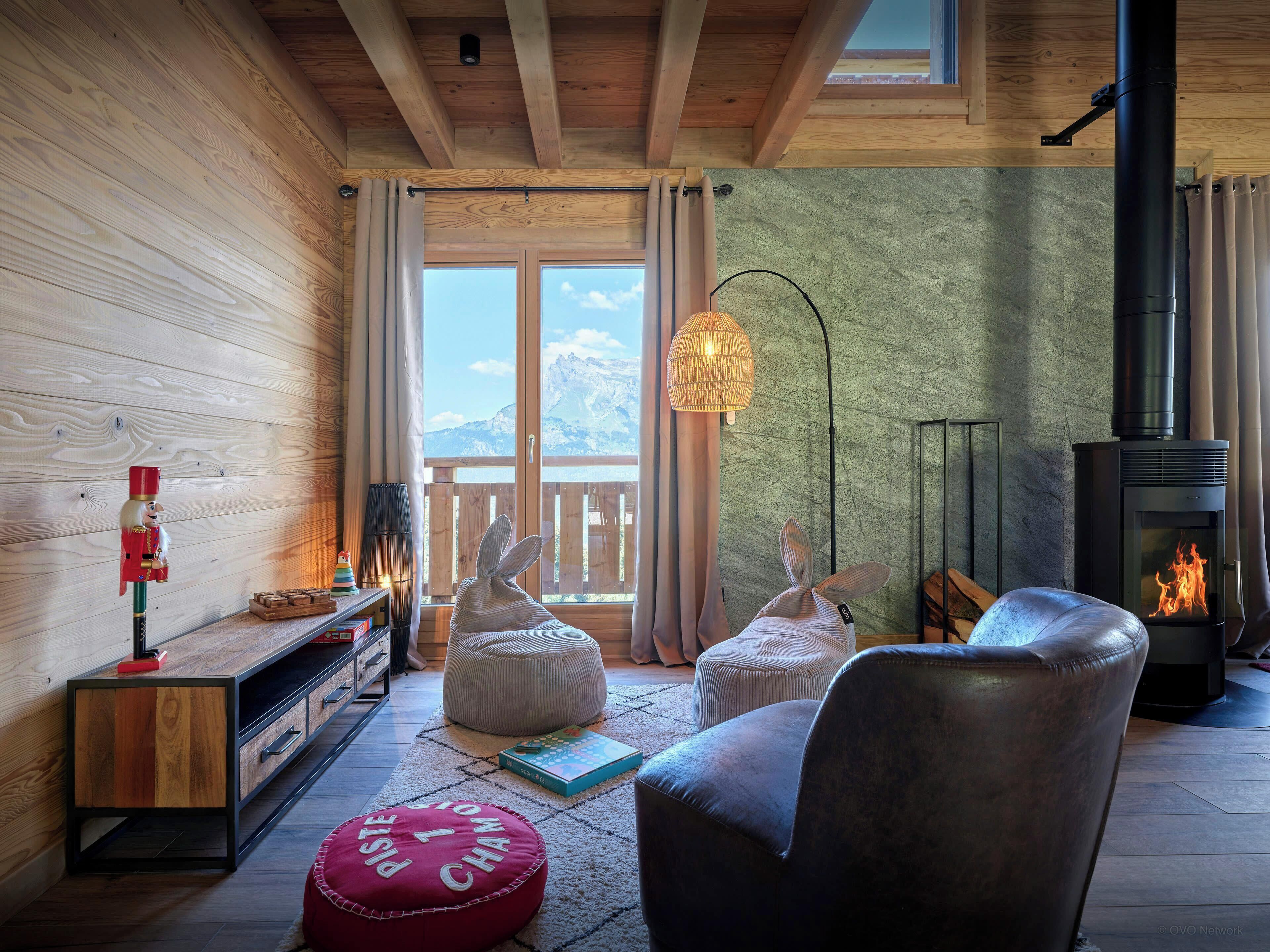 A cozy living room with a fireplace, wooden walls, and a view of the mountains.