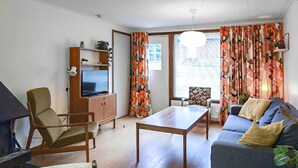 Sala de estar com sofá, mesa de madeira, televisão em um móvel e uma cadeira.