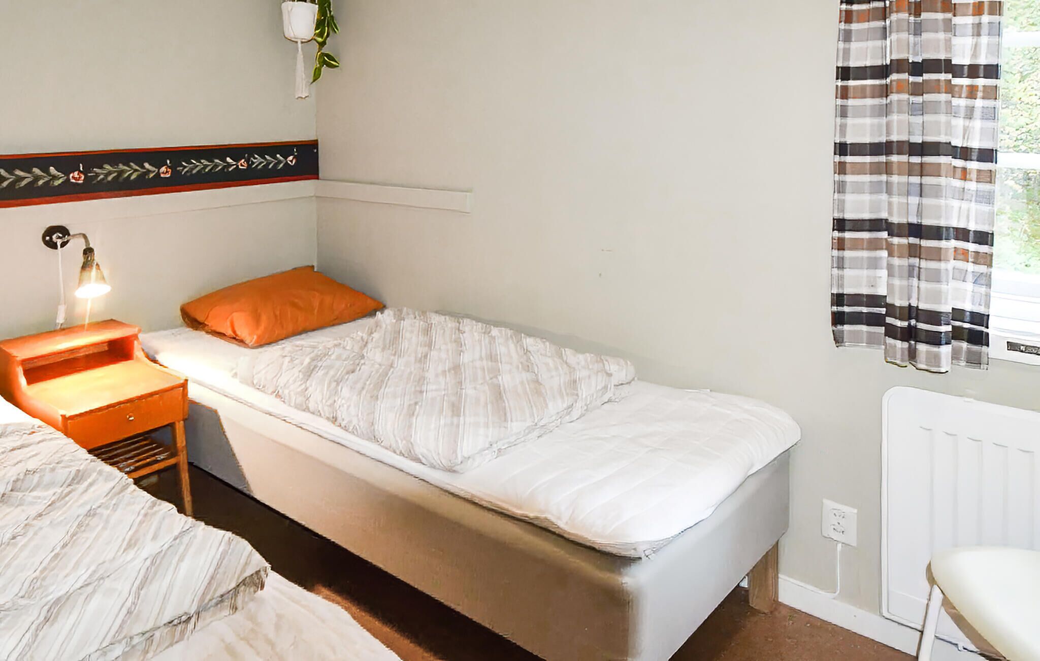 Una camera da letto piccola e ordinata con un letto singolo, un comodino con una lampada, un termosifone e una finestra con tende.
