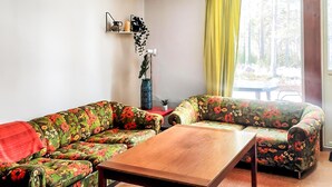 Un salon avec des canapés à motifs floraux, une table basse en bois, une petite table d’appoint et une plante en pot.