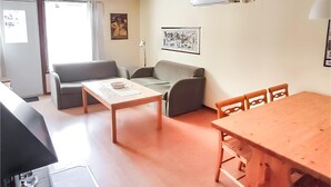 En moderne stue med sofa, spisebord og sofabord. To stole står ved bordet, og en lampe er placeret på et sengebord.