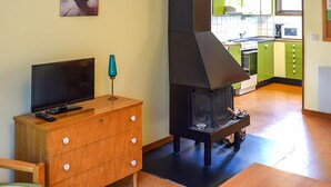 A living room with a TV on a wooden dresser, a fireplace, and a kitchen in the background. - 2 bedroom nice home in Ekshärad (Ekshärad)
