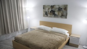 Una camera da letto con un letto di legno, cuscini bianchi, un comodino, una lampada da terra e un quadro appeso al muro.